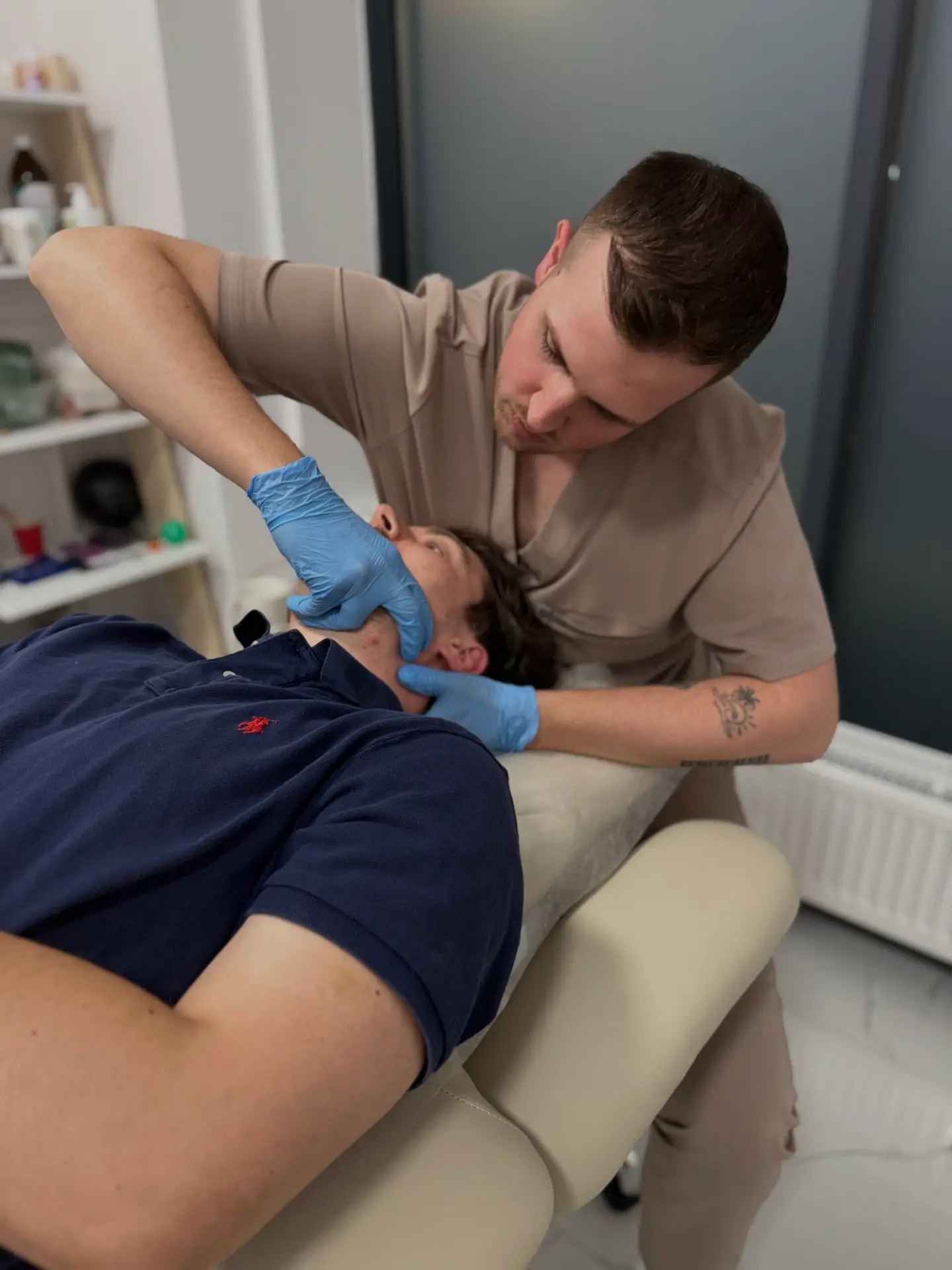 Fizjoterapeuta wykonujący terapię manualną okolic szyi i żuchwy pacjenta leżącego na stole rehabilitacyjnym.
