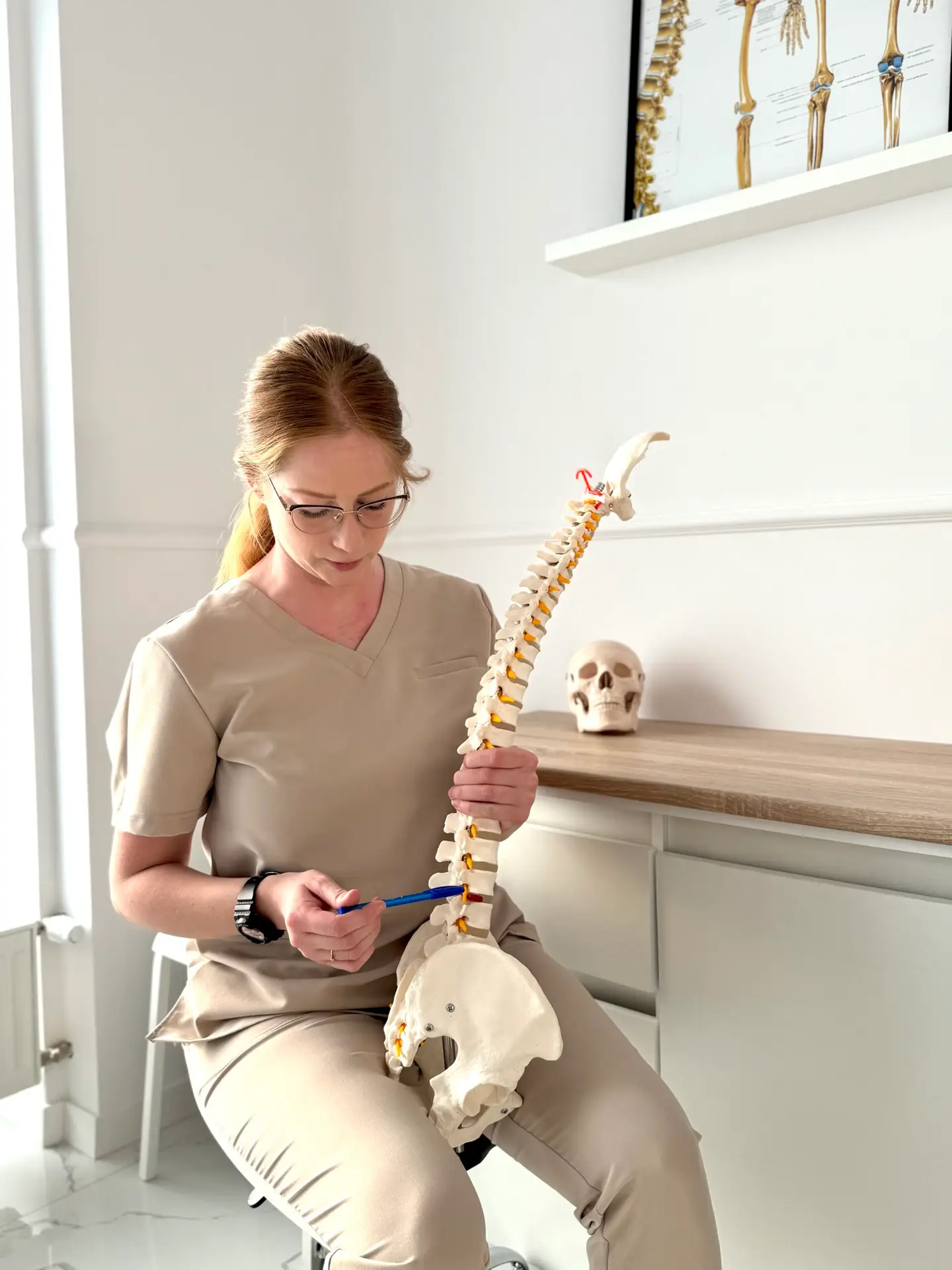 Fizjoterapeutka w gabinecie Fizjocare wskazująca na odcinek lędźwiowy na anatomicznym modelu kręgosłupa.